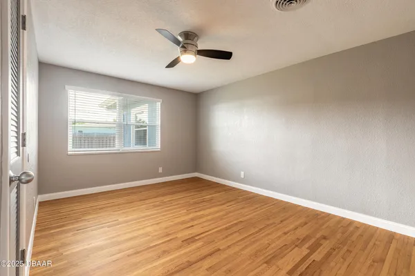 a view of empty room with wooden floor and fan