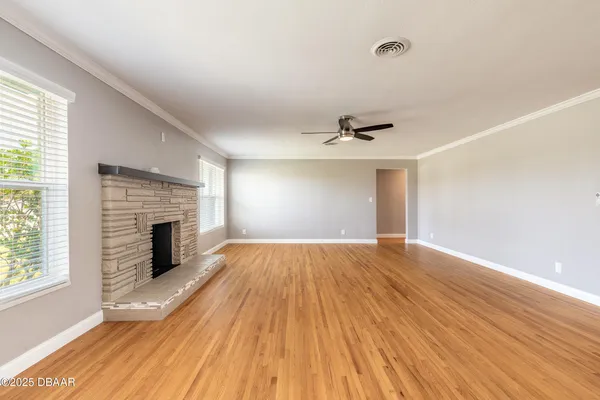 an empty room with wooden floor fireplace and windows
