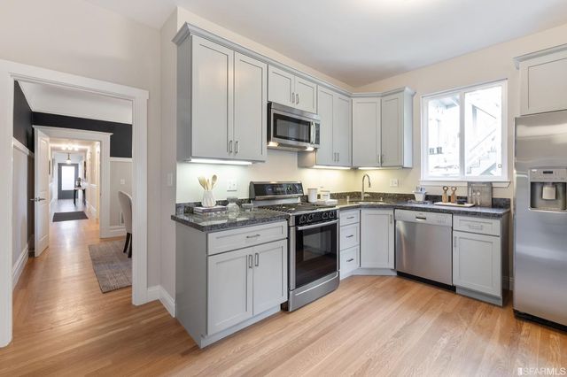 a kitchen with stainless steel appliances granite countertop a stove top oven a sink dishwasher a refrigerator and a microwave oven on the wooden floor