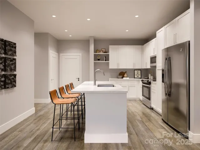 a kitchen with stainless steel appliances a refrigerator a stove a sink and a dining table with wooden floor