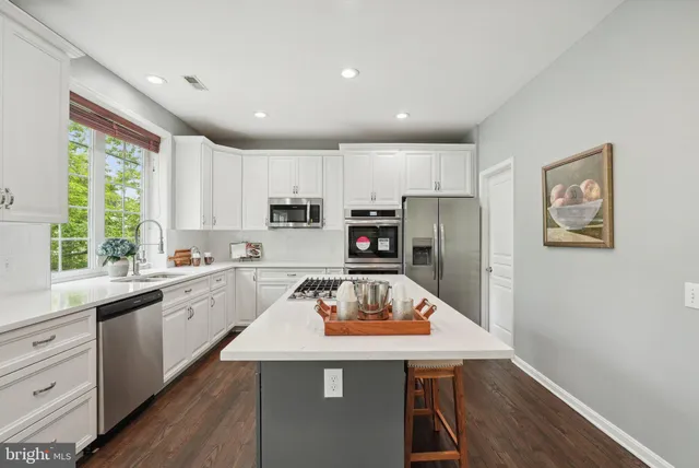 a open dining room with stainless steel appliances a dining table wooden floor and a large window
