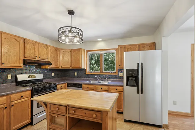 a kitchen with stainless steel appliances granite countertop a refrigerator a sink dishwasher a stove and a dining table with wooden floor