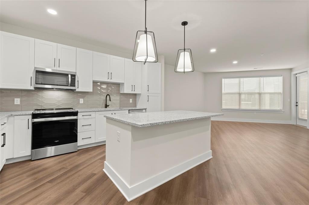2648 Sandy Plains Road, Unit 420 Marietta, GA 30062 - Photo 2 of 37 a kitchen with kitchen island granite countertop a stove a sink and white cabinets with wooden floor