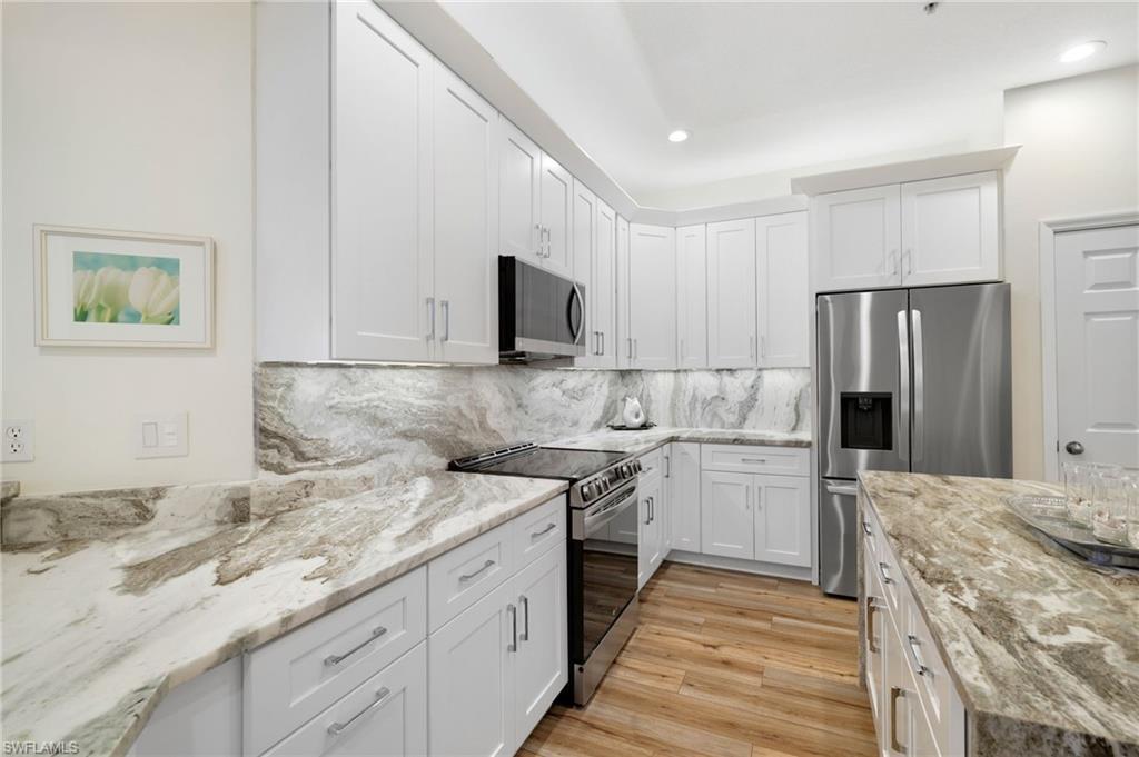 Kitchen with appliances with stainless steel finishes, tasteful backsplash, light stone counters, light wood finished floors, and white cabinets