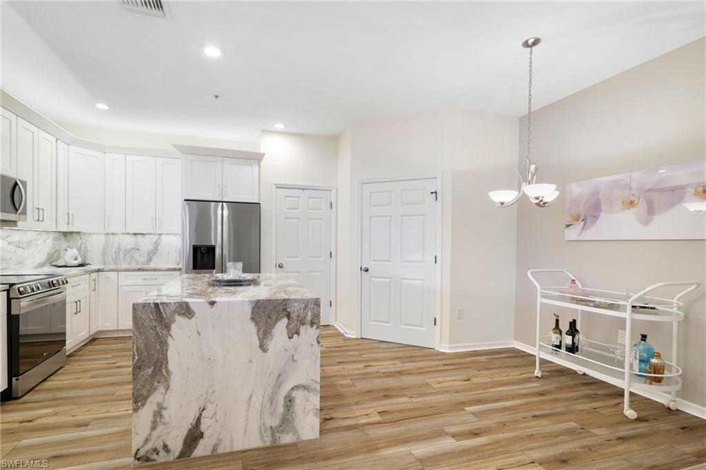 3787 Costa Maya Way, Unit 101 Estero, FL 33928 - Photo 14 of 49 Kitchen featuring appliances with stainless steel finishes, tasteful backsplash, light stone counters, white cabinets, and hanging light fixtures