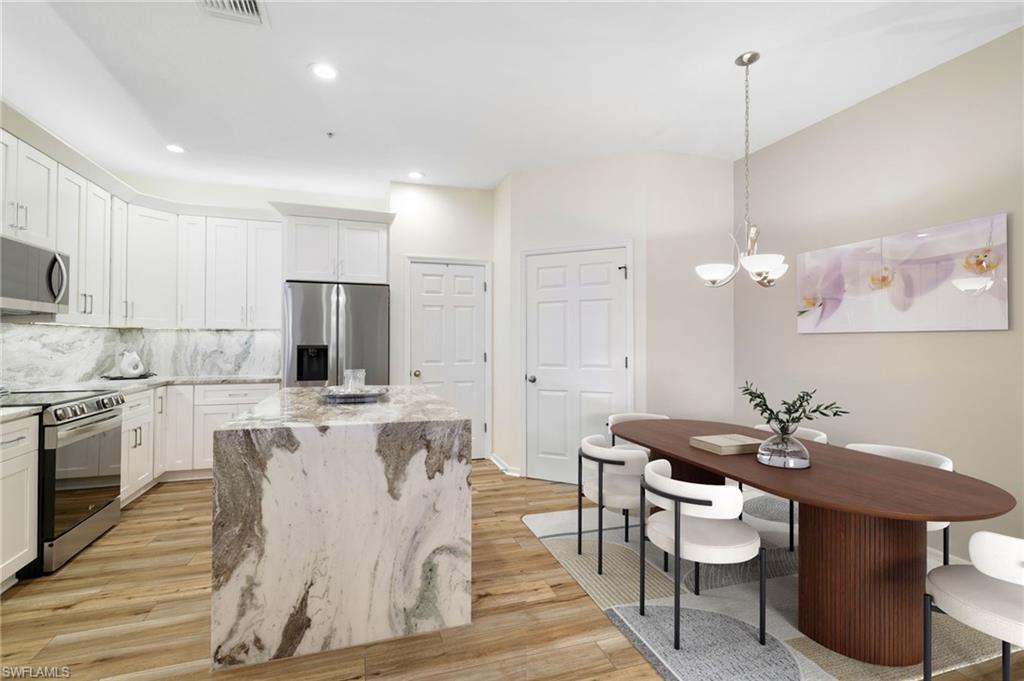 3787 Costa Maya Way, Unit 101 Estero, FL 33928 - Photo 15 of 49 Kitchen with appliances with stainless steel finishes, light stone countertops, white cabinetry, hanging light fixtures, and light wood finished floors