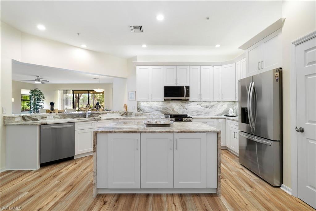 3787 Costa Maya Way, Unit 101 Estero, FL 33928 - Photo 16 of 49 Kitchen with appliances with stainless steel finishes, white cabinetry, a center island, light wood-type flooring, and decorative backsplash