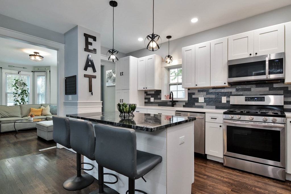 15 Balcomb Street Salem, MA 01970 - Photo 8 of 42 a kitchen with stainless steel appliances granite countertop a stove a sink dishwasher a dining table and chairs with wooden floor