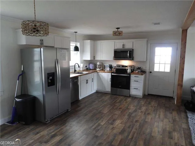 a kitchen with stainless steel appliances granite countertop a stove top oven a sink dishwasher a refrigerator and a dining table with wooden floor