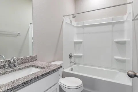 a bathroom with a granite countertop bathtub shower sink vanity and toilet