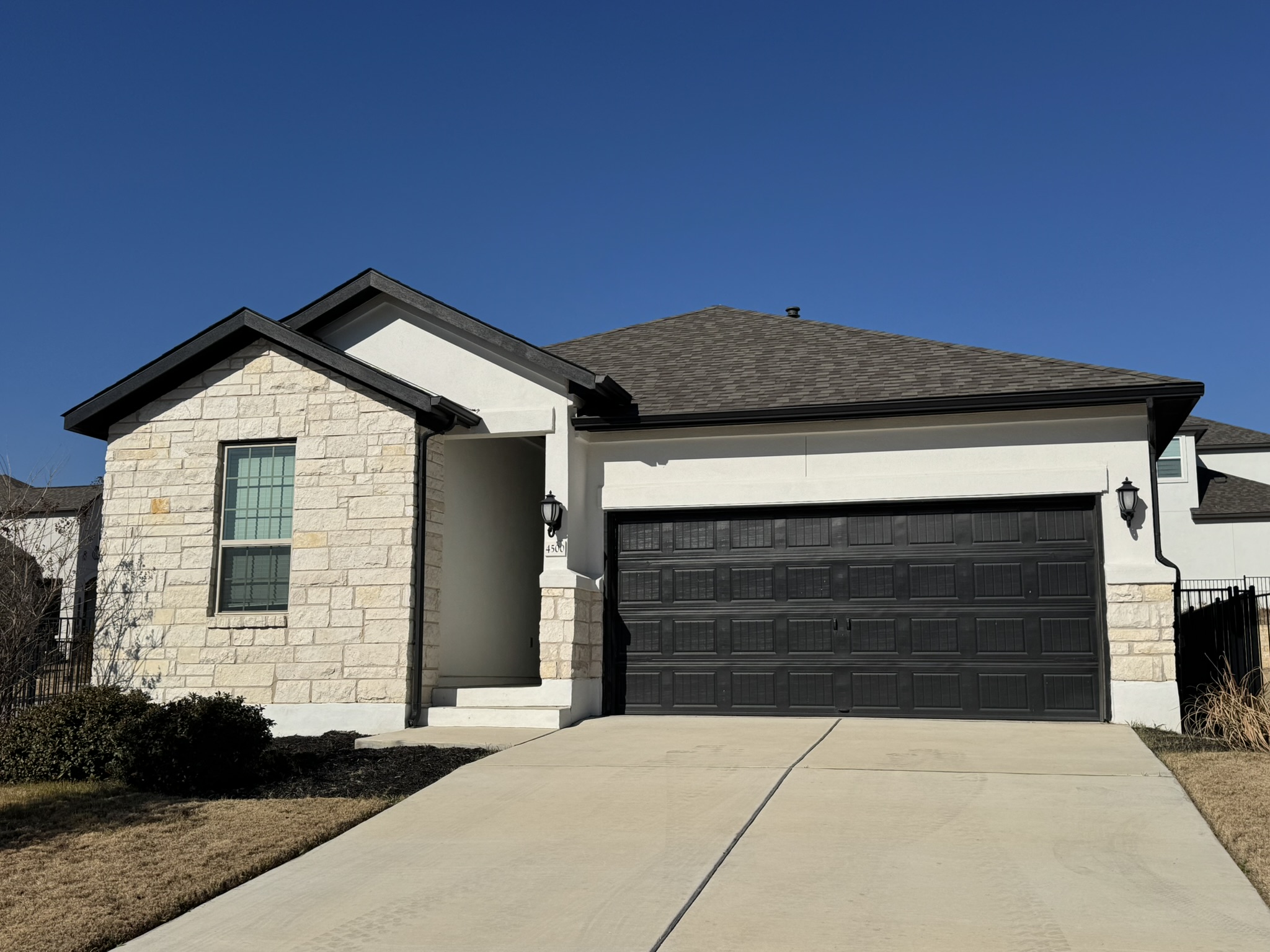 Ranch-style house with stone siding, a garage, driveway, stucco siding, and roof with shingles