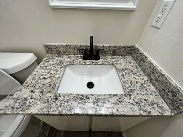 a bathroom with a granite countertop sink and a toilet