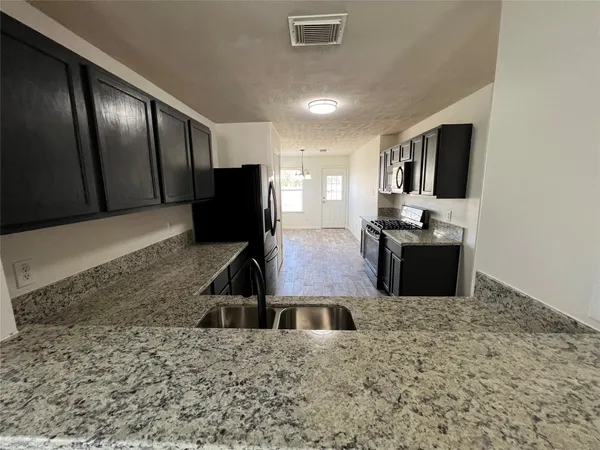 a kitchen with stainless steel appliances kitchen island granite countertop a refrigerator a stove and a sink with large countertops