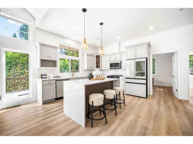 a kitchen with stainless steel appliances kitchen island granite countertop a refrigerator a stove a sink dishwasher a dining table and chairs with wooden floor