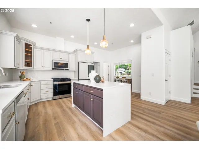 a large kitchen with stainless steel appliances kitchen island granite countertop a stove a sink a refrigerator white cabinets and wooden floor