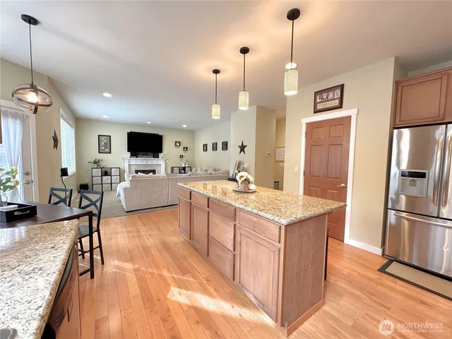 a large kitchen with stainless steel appliances kitchen island granite countertop a refrigerator a stove top oven a sink a dining table and chairs with wooden floor