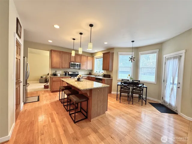 a open kitchen with stainless steel appliances granite countertop a stove top oven a refrigerator a dining table and chairs with wooden floor