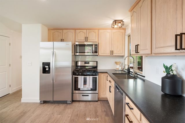 a kitchen with granite countertop a refrigerator a sink a stove and wooden floors