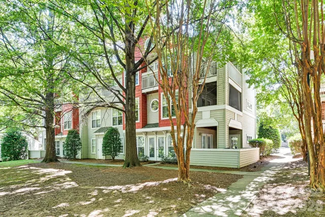 a view of a white house next to a yard with large trees
