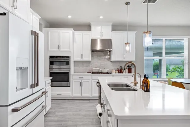 a kitchen with stainless steel appliances white cabinets a sink a stove a refrigerator and cabinets