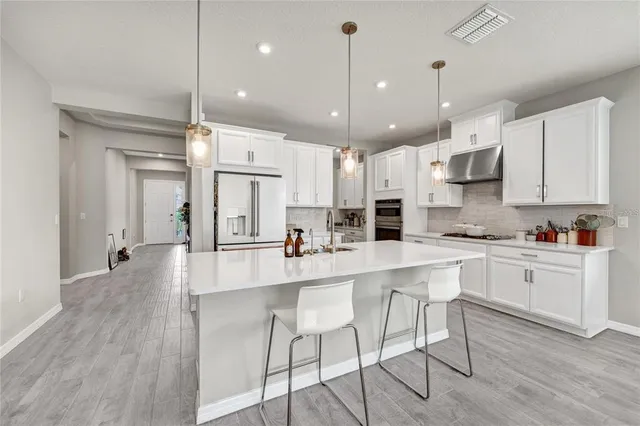 a large kitchen with stainless steel appliances kitchen island granite countertop a stove a refrigerator a oven and white cabinets with wooden floor