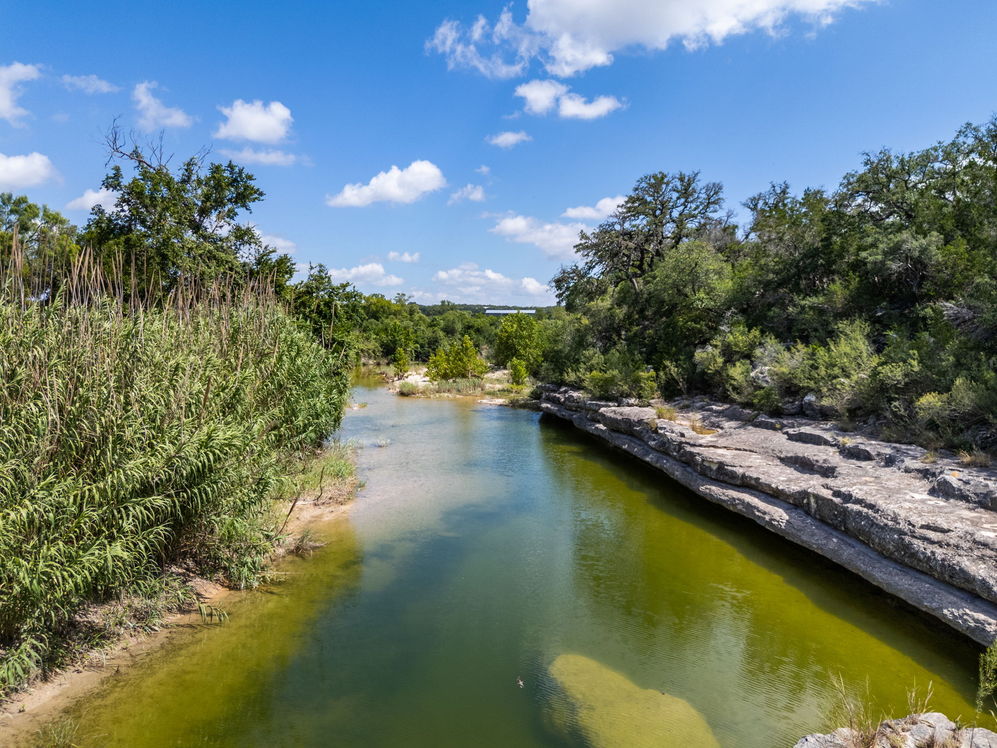 5385 Ranch Road 165 Blanco, TX 78606 - Photo 2 of 40 A tranquil water feature meanders through lush natural landscaping, showcasing a serene outdoor retreat.