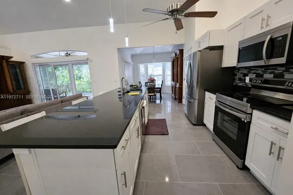 a kitchen with stainless steel appliances granite countertop a sink a stove a refrigerator a washer dryer and a dining table with wooden floor