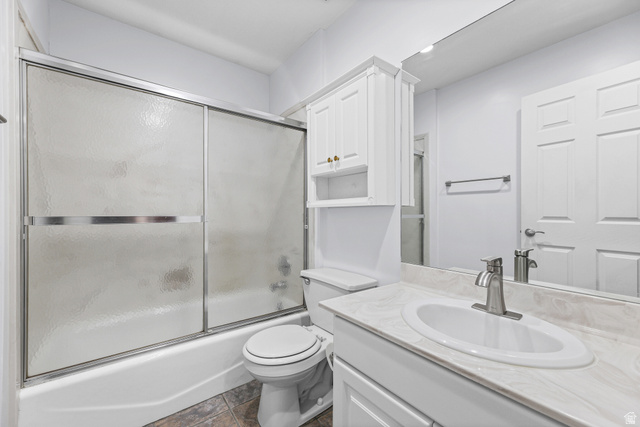 4117 North Wolf Ridge Circle Eden, UT 84310 - Photo 27 of 63 Bathroom featuring a full-size tub with sliding frosted glass doors, a vanity with an integrated sink and light-toned countertop, a wall-mounted medicine cabinet with gold-toned hardware, and mosaic-style floor tiling