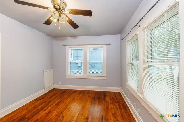 a view of an empty room with wooden floor and a window