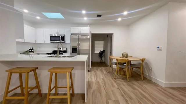 a kitchen with stainless steel appliances granite countertop a dining table chairs refrigerator and sink