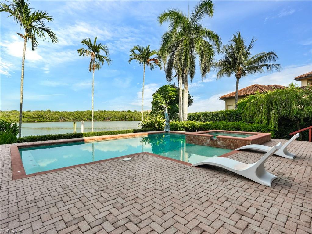 2535 Tarpon Road Naples, FL 34102 - Photo 42 of 50 Mediterranean-style exterior featuring a spacious pool, integrated spa with stone detailing, extensive tiled patio, arched covered patio, and a second-story balcony with iron railing