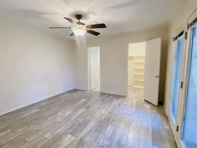 an empty room with wooden floor fan and windows