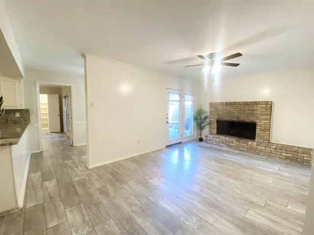 an empty room with wooden floor fireplace and a kitchen view