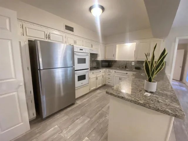 a kitchen with granite countertop a refrigerator a stove a sink and white cabinets