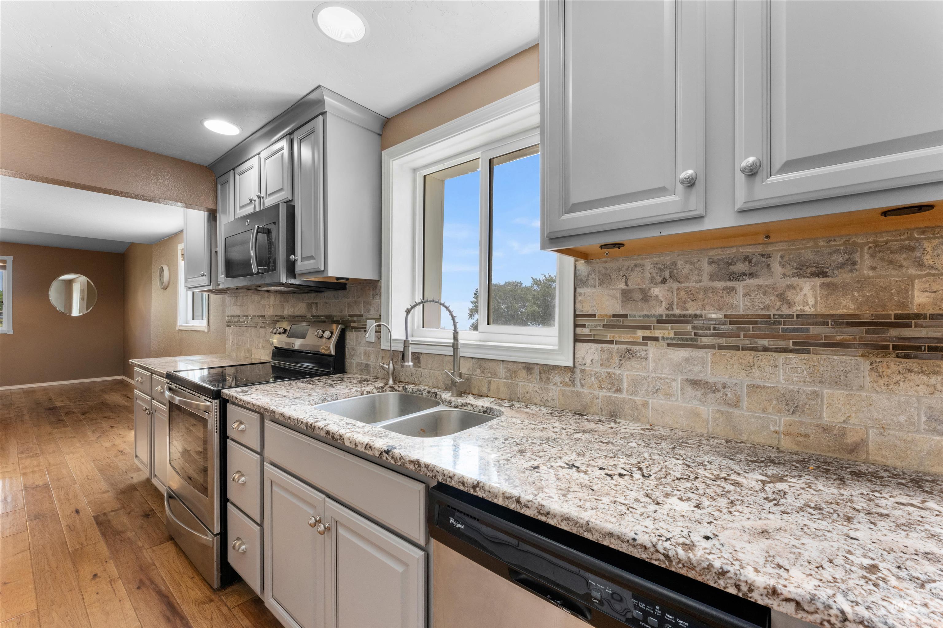 17441 Upper Pleasant Ridge Road Caldwell, ID 83607 - Photo 13 of 40 Kitchen featuring light-toned cabinetry, granite countertops, stainless steel appliances, a tiled backsplash with a decorative accent band, and wood-finish flooring