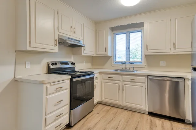 a kitchen with stainless steel appliances granite countertop white cabinets a sink and dishwasher with wooden floor