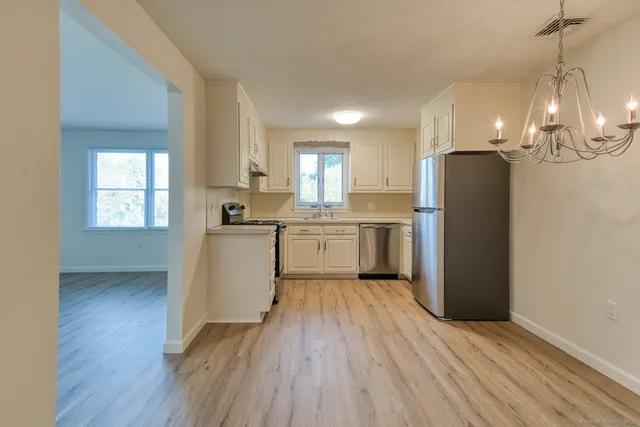 a kitchen with stainless steel appliances granite countertop a refrigerator a sink dishwasher a stove and white countertops with wooden floor