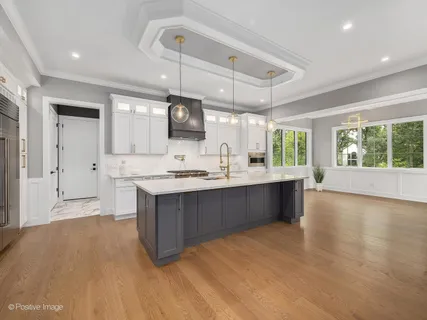 a large kitchen with stainless steel appliances a large counter top a stove a sink dishwasher a refrigerator and a dining table with wooden floor