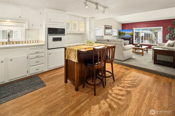 a kitchen with stainless steel appliances kitchen island granite countertop a stove a sink dishwasher and white cabinets with wooden floor