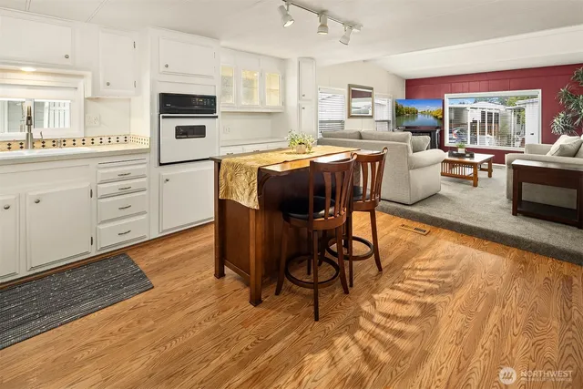 a kitchen with stainless steel appliances kitchen island granite countertop a stove a sink dishwasher and white cabinets with wooden floor