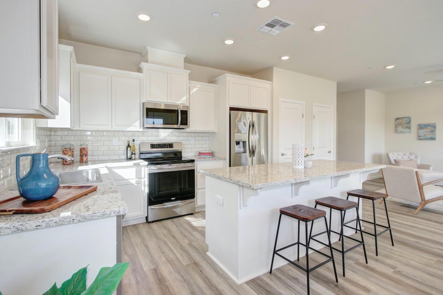 a kitchen with granite countertop a stove a sink a microwave a refrigerator and white cabinets with wooden floor