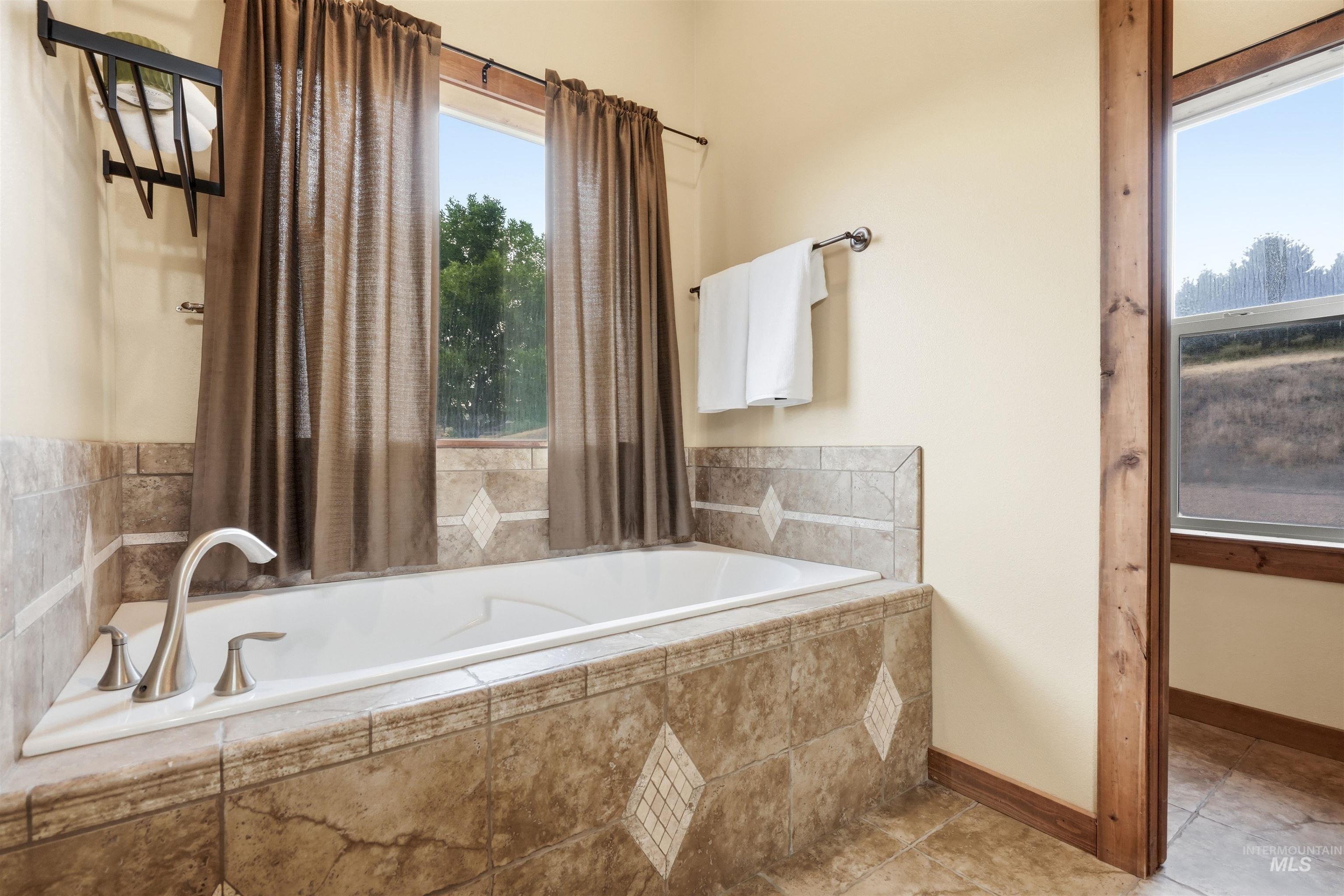 3645 Butte Road Emmett, ID 83617 - Photo 21 of 39 Soaking tub with brushed nickel fixtures, surrounded by tile with decorative inlays, and set beneath a window