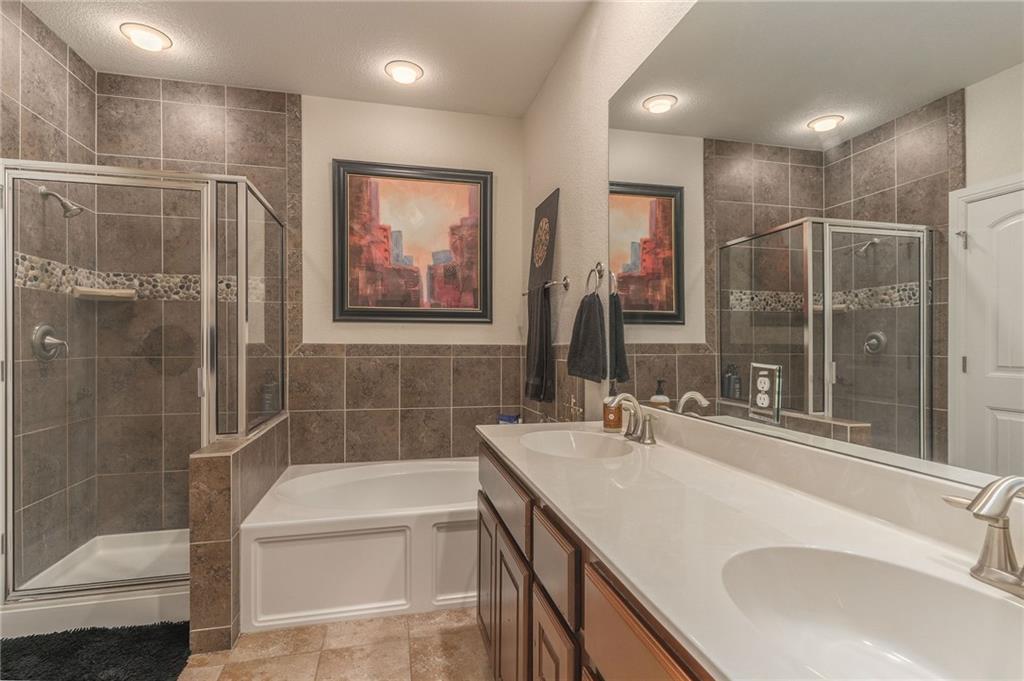 6708 Menchaca Road, Unit 14 Austin, TX 78745 - Photo 5 of 22 Bathroom featuring a glass-enclosed shower, a separate built-in soaking tub, a dual vanity with integrated sinks, a large wall-mounted mirror, and tile flooring