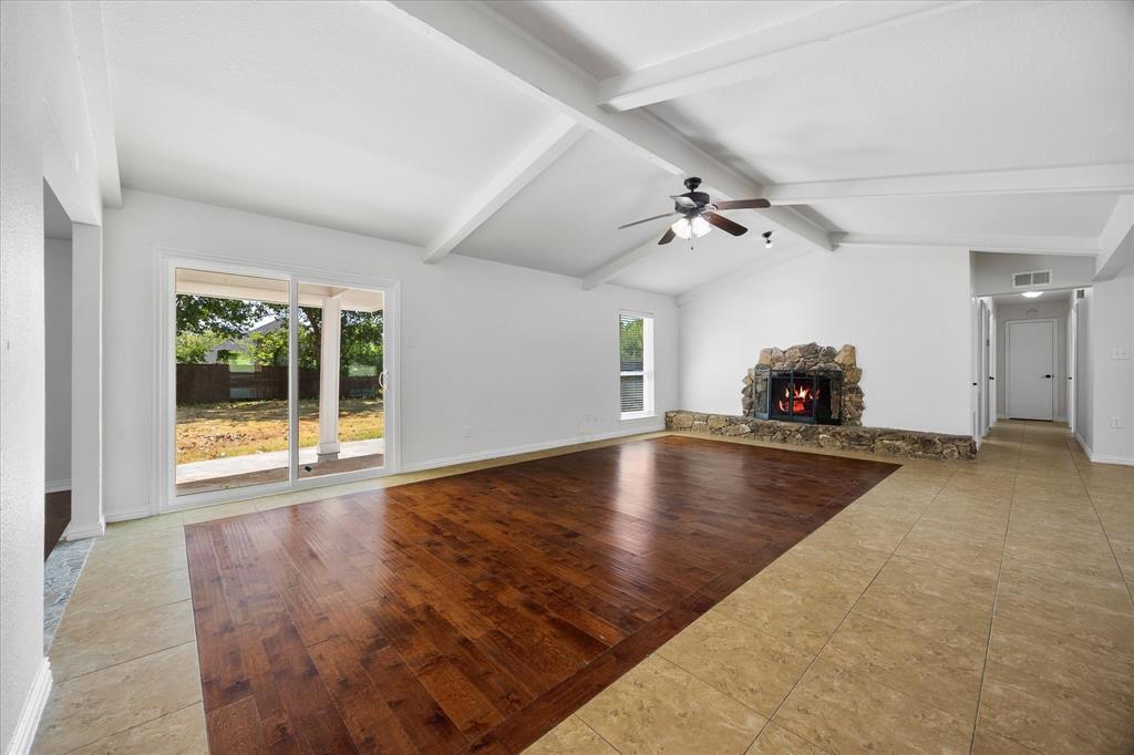 925 Lake North Road Rowlett, TX 75089 - Photo 11 of 37 Vaulted ceiling with exposed beams, stone fireplace, wood-finish flooring, tiled flooring, and sliding glass door to the exterior