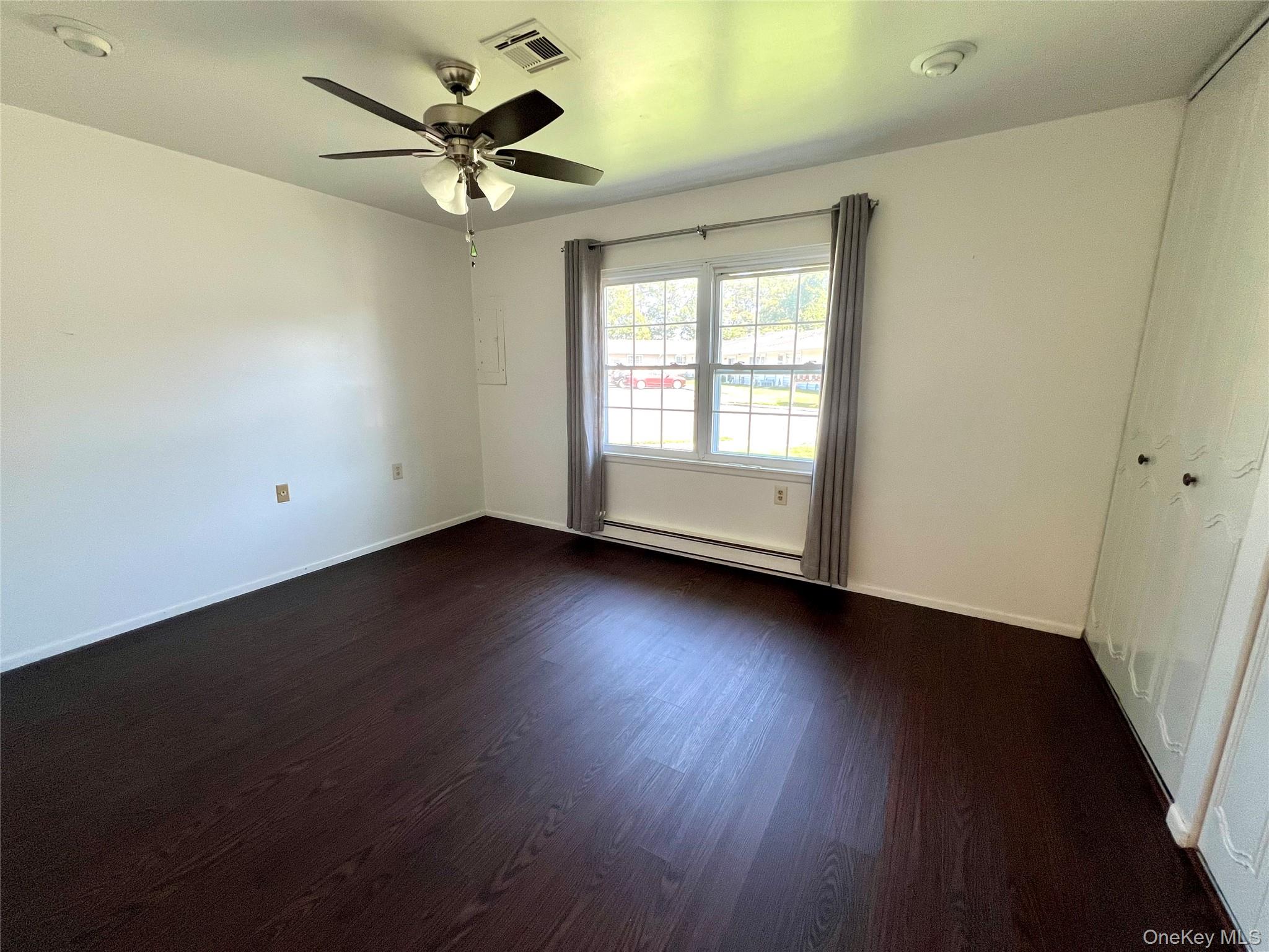 171 B Ventry Court, Unit 171B Ridge, NY 11961 - Photo 13 of 19 an empty room with wooden floor and windows with curtains