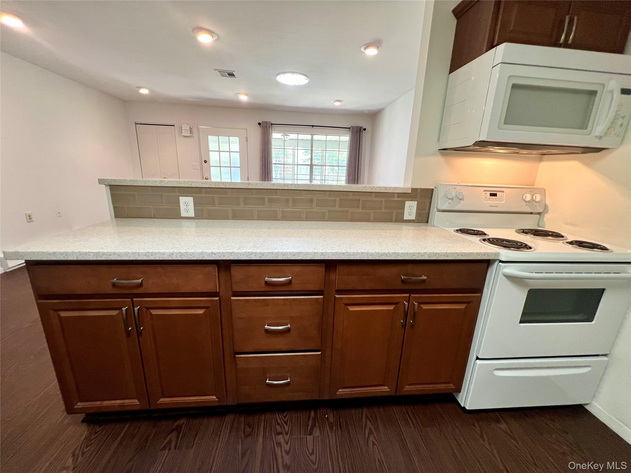 171 B Ventry Court, Unit 171B Ridge, NY 11961 - Photo 7 of 19 a kitchen with kitchen island granite countertop wooden cabinets and white appliances