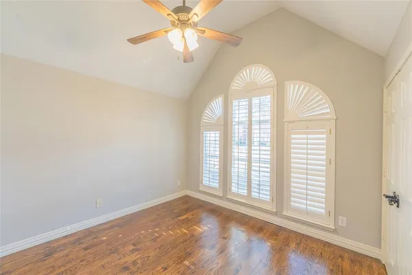 an empty room with wooden floor fan and windows