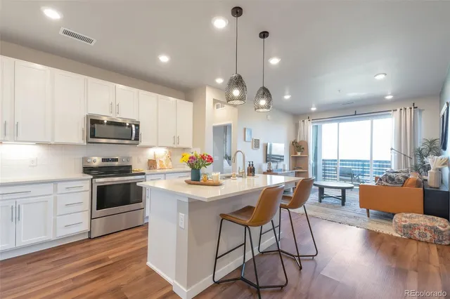 a kitchen with stainless steel appliances kitchen island granite countertop a stove top oven a sink dishwasher a dining table and chairs with wooden floor