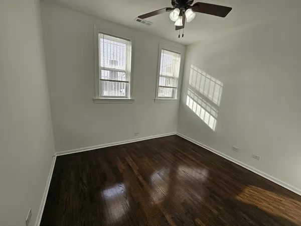 an empty room with wooden floor fan and windows