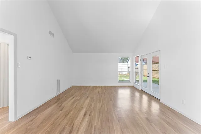 a view of an empty room with wooden floor and window